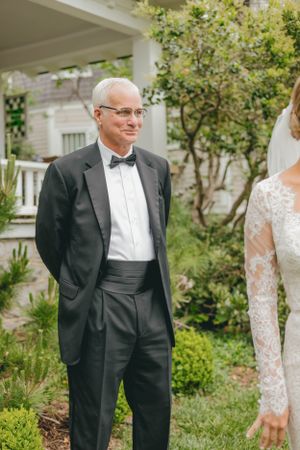 Father in tuxedo smiling proudly as he sees his daughter in wedding dress for first time.