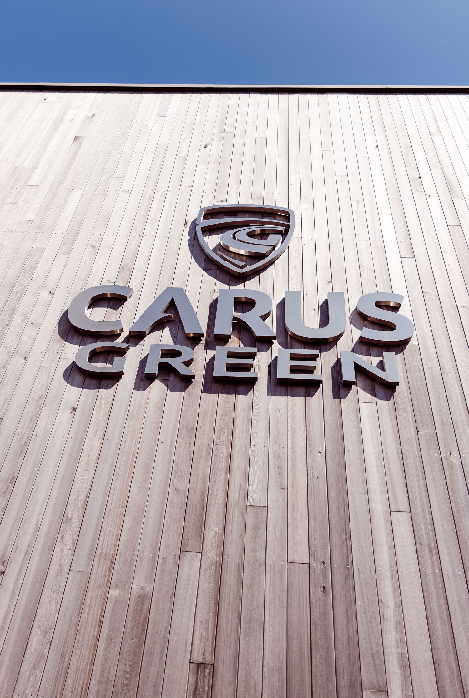 Wooden wall with Carus Creek logo mounted in dark brown lettering.
