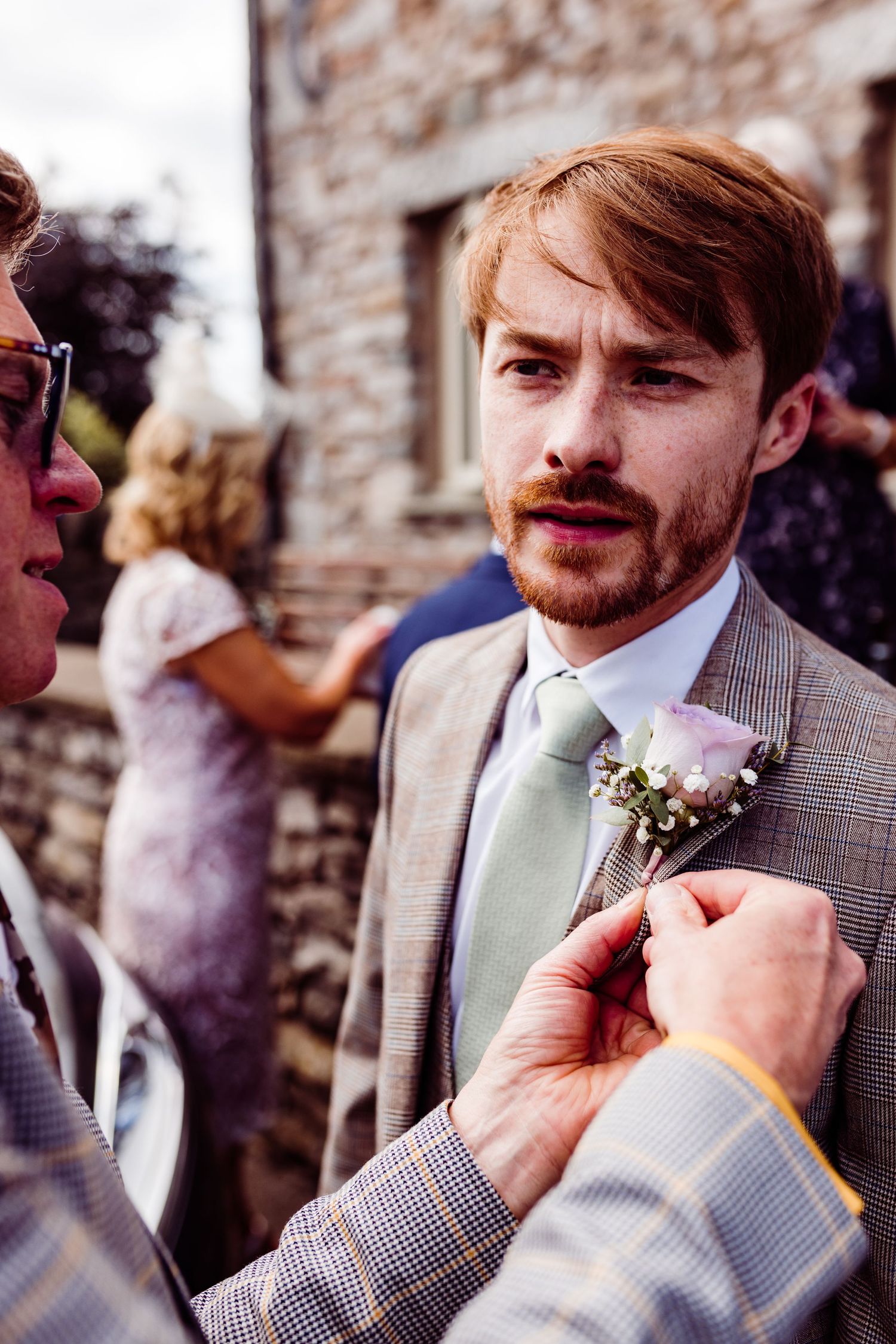 Boutonniere being pinned on light grey suit jacket at outdoor wedding.