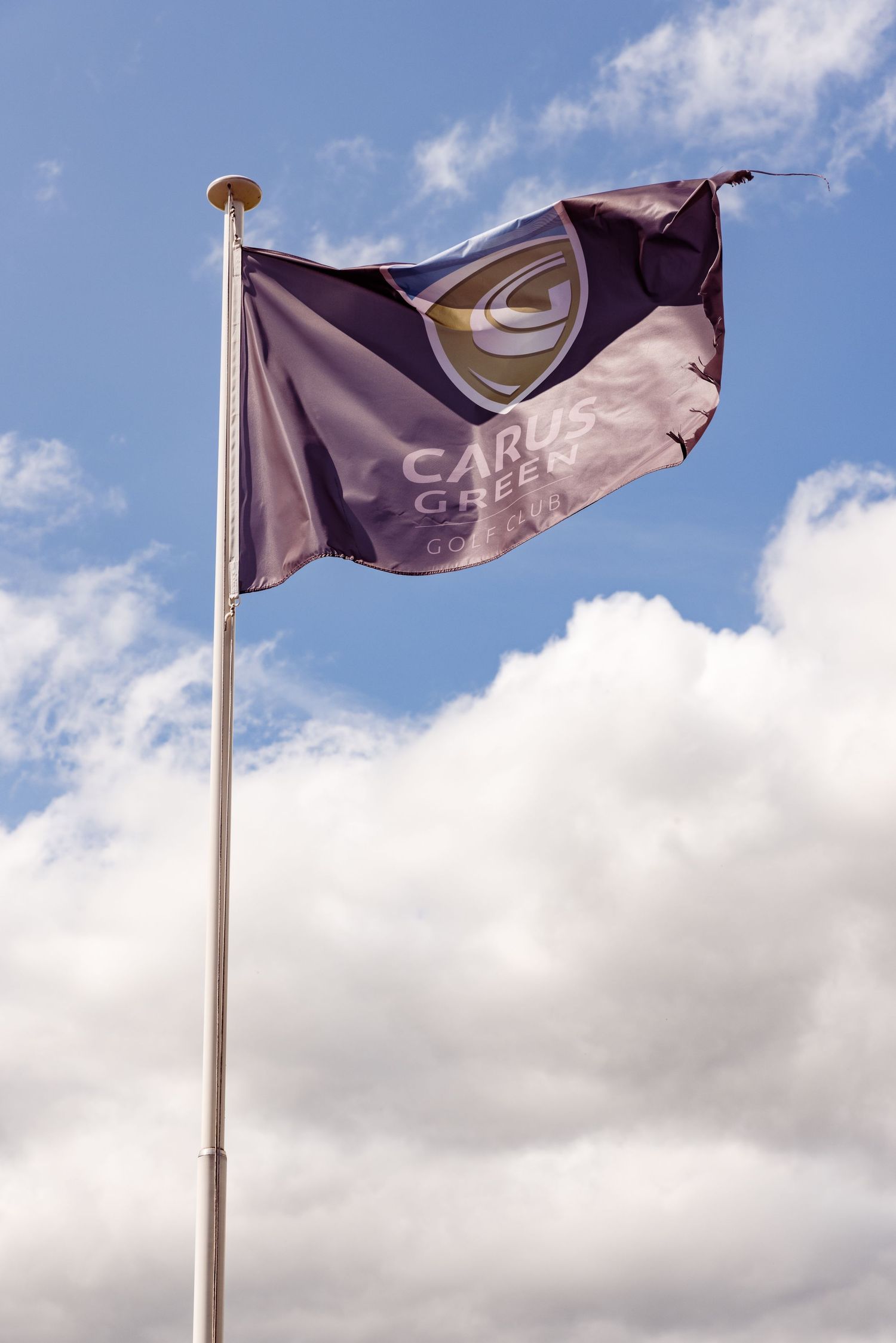Carus Creek flag waves against blue sky with white clouds.