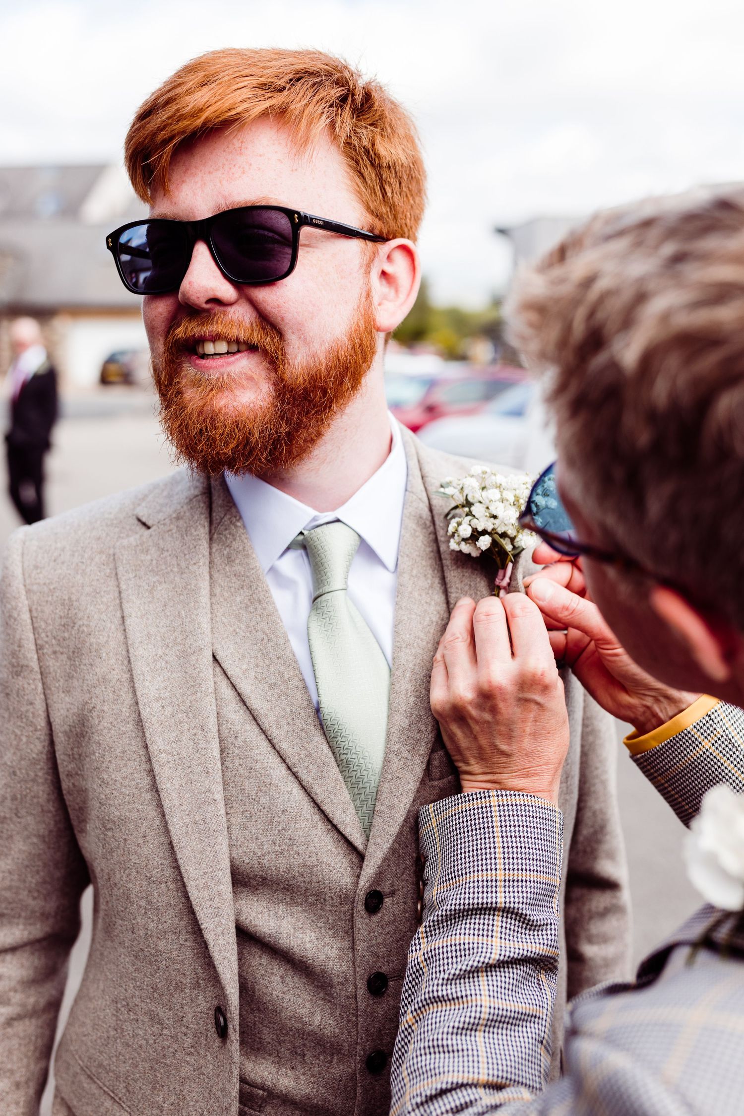 Someone adjusting a white floral boutonniere on light grey wedding suit.