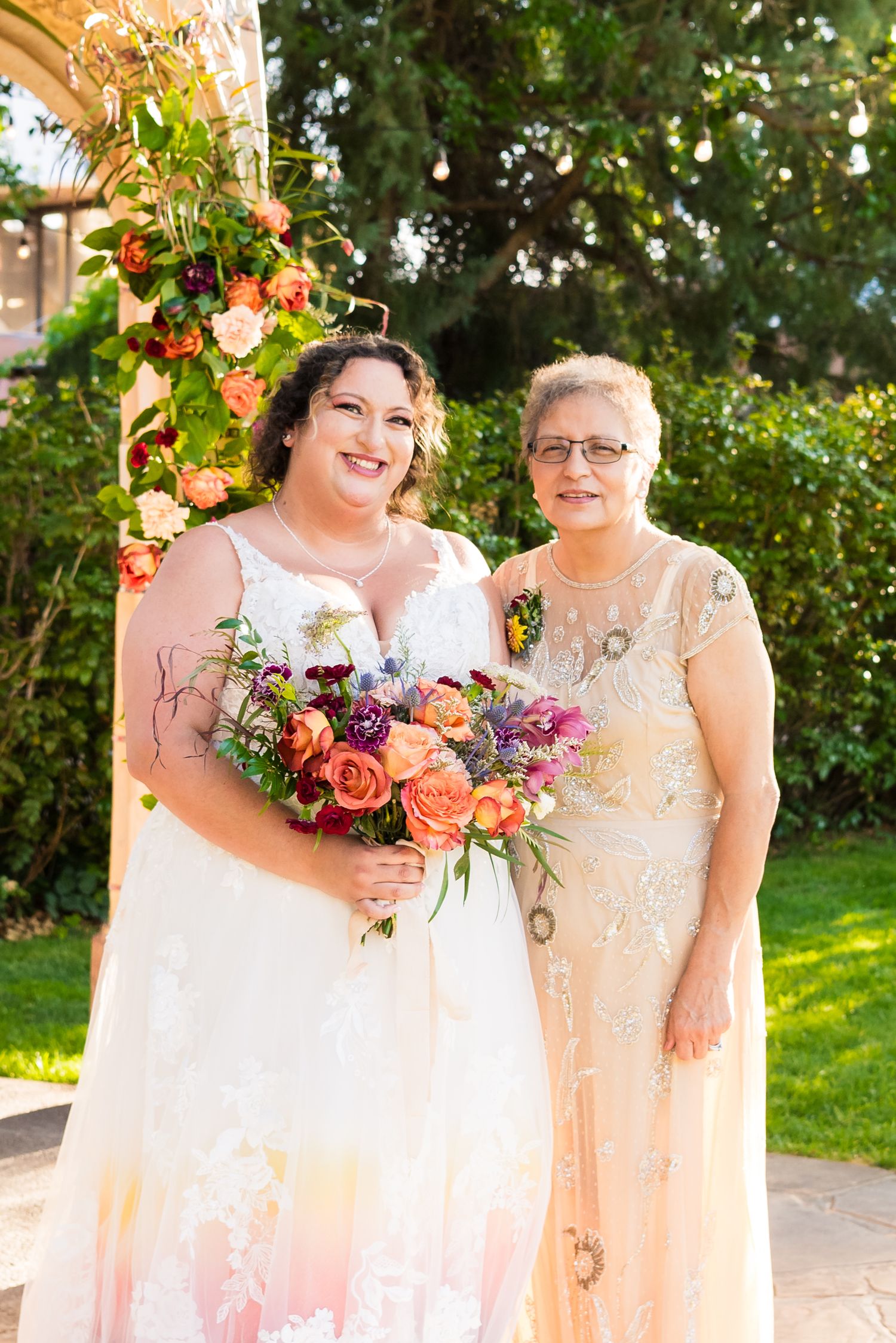 Bride posing with her mother in a lush garden courtyard for family formals.
