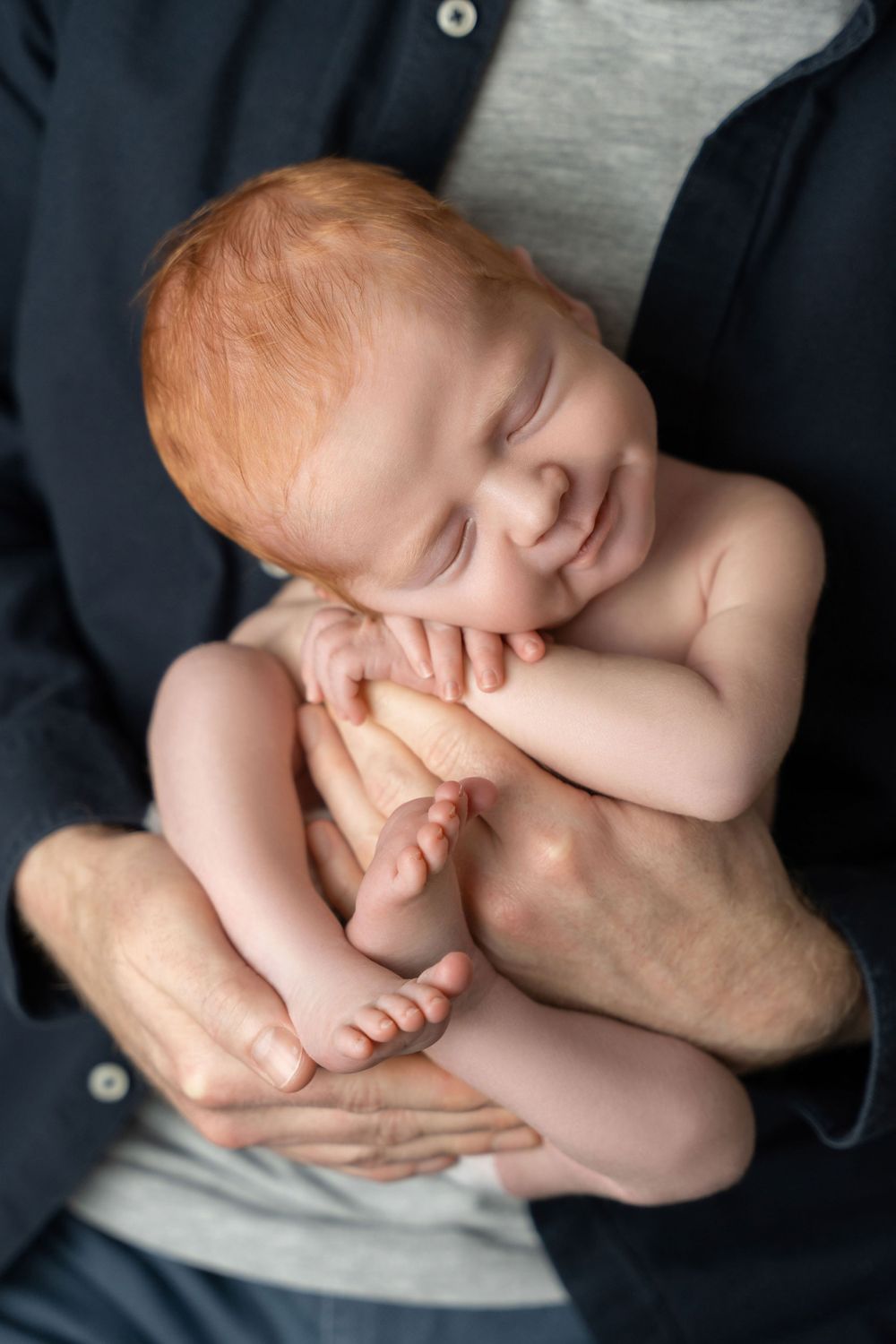 Smiling baby being held gently during a tender portrait session.