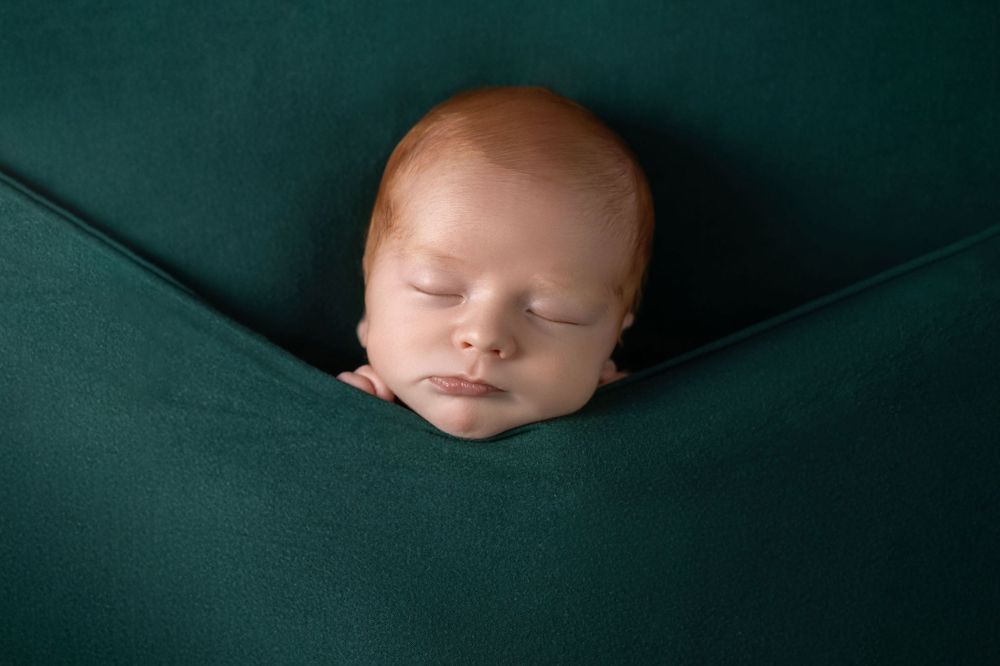 Newborn baby sleeping peacefully nestled in dark green fabric.