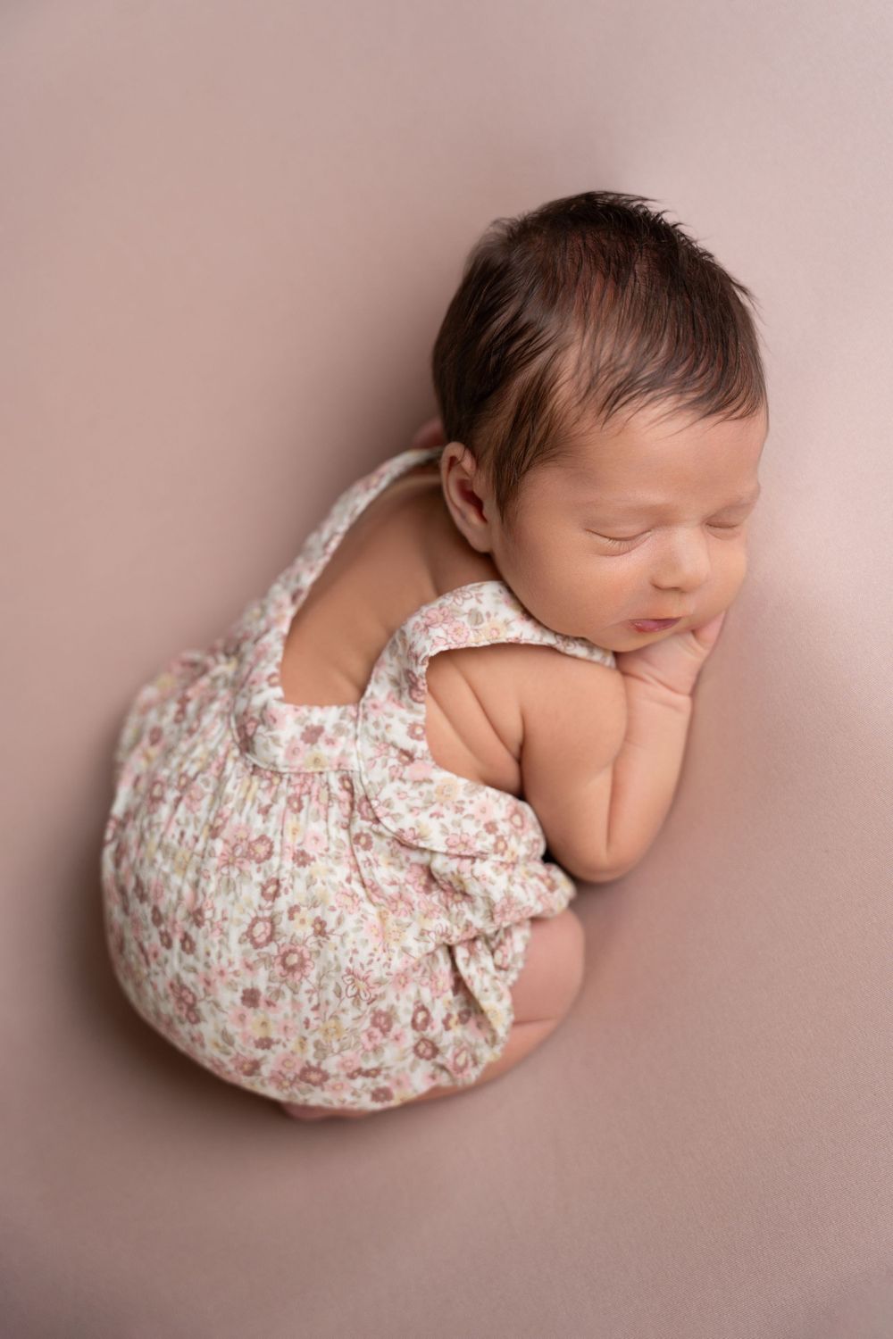 Sleeping newborn in floral outfit posed on pink background.