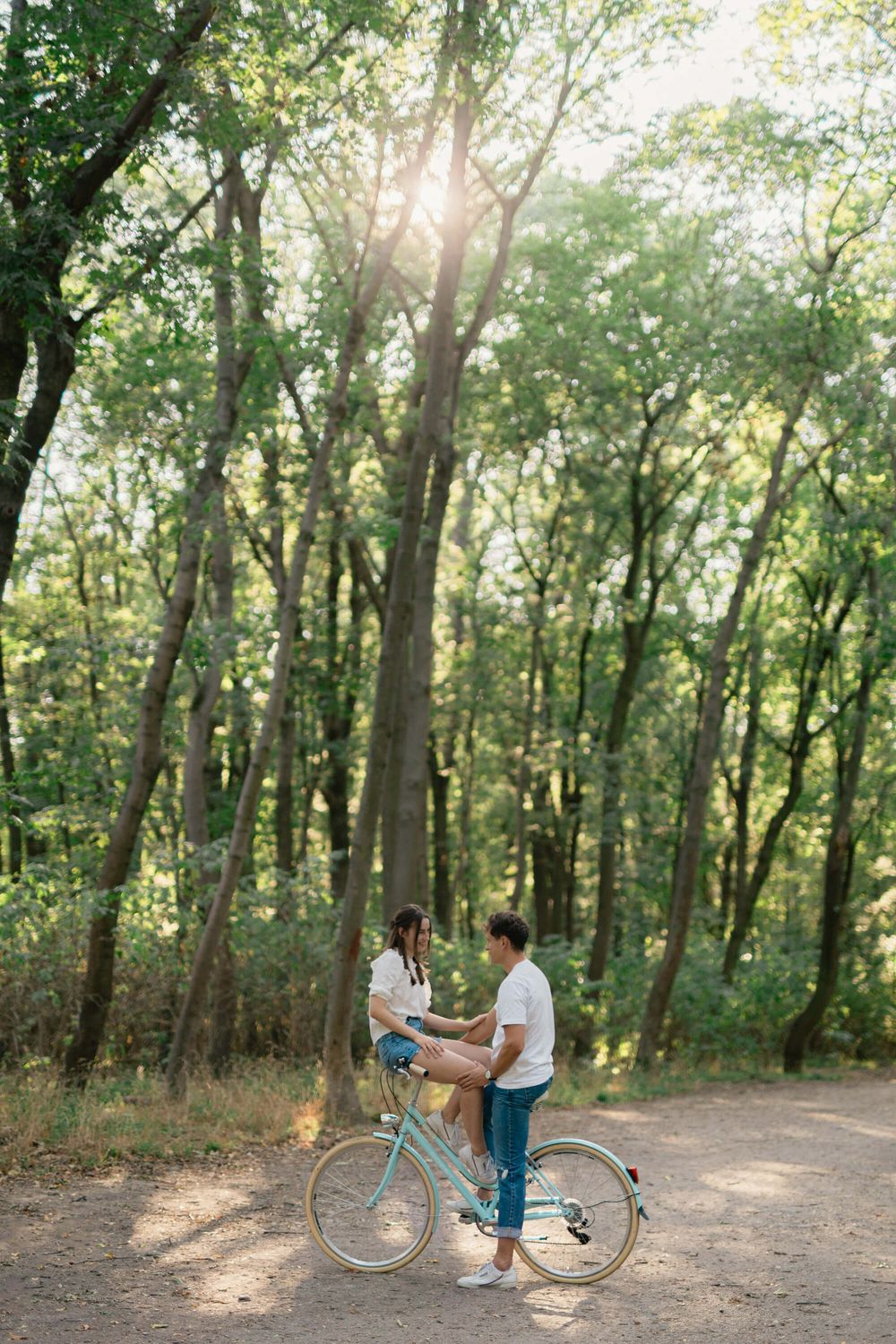 Romantic forest scene with couple sharing a vintage bicycle on a sunlit trail.