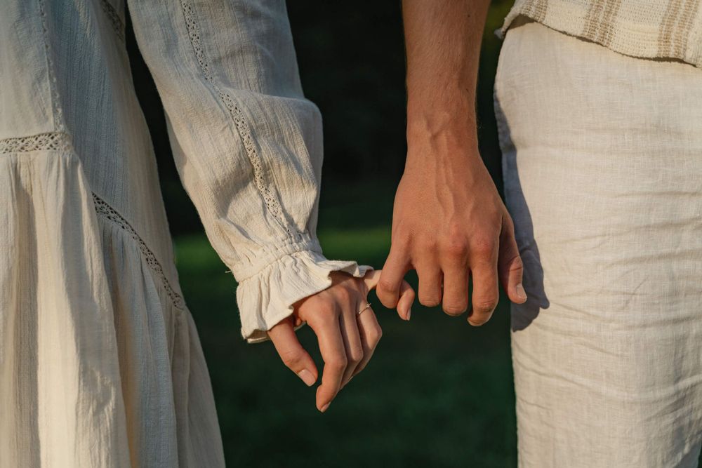 Close-up of hands gently touching while wearing white linen clothing.