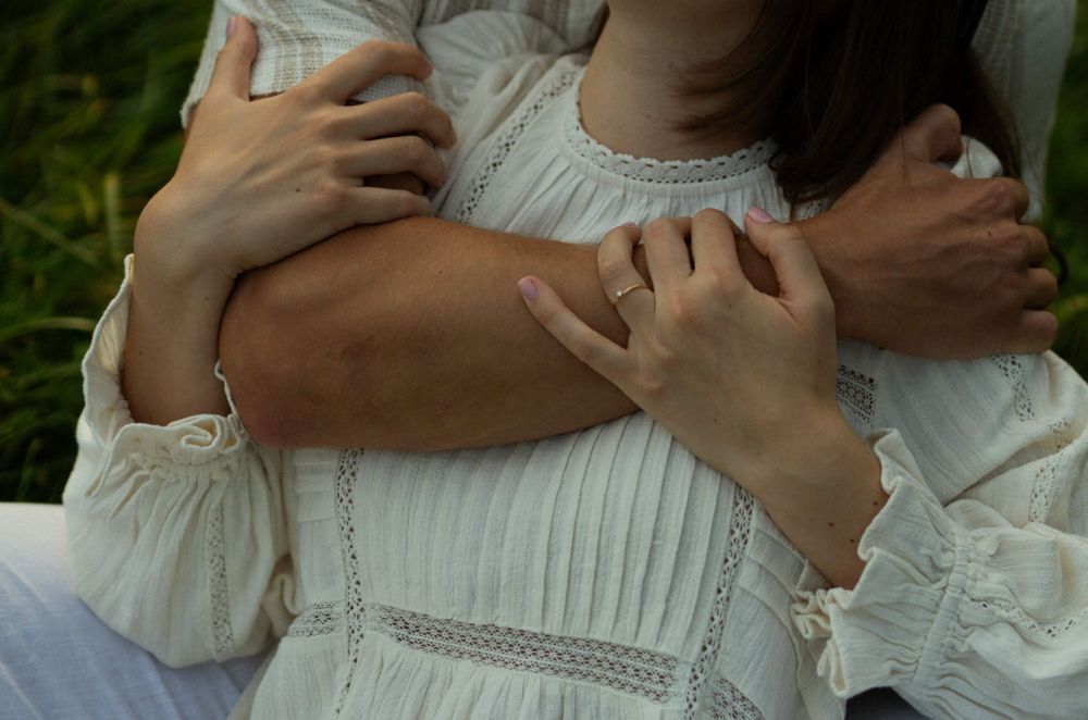Arms embracing in white vintage-style clothing against a natural background.
