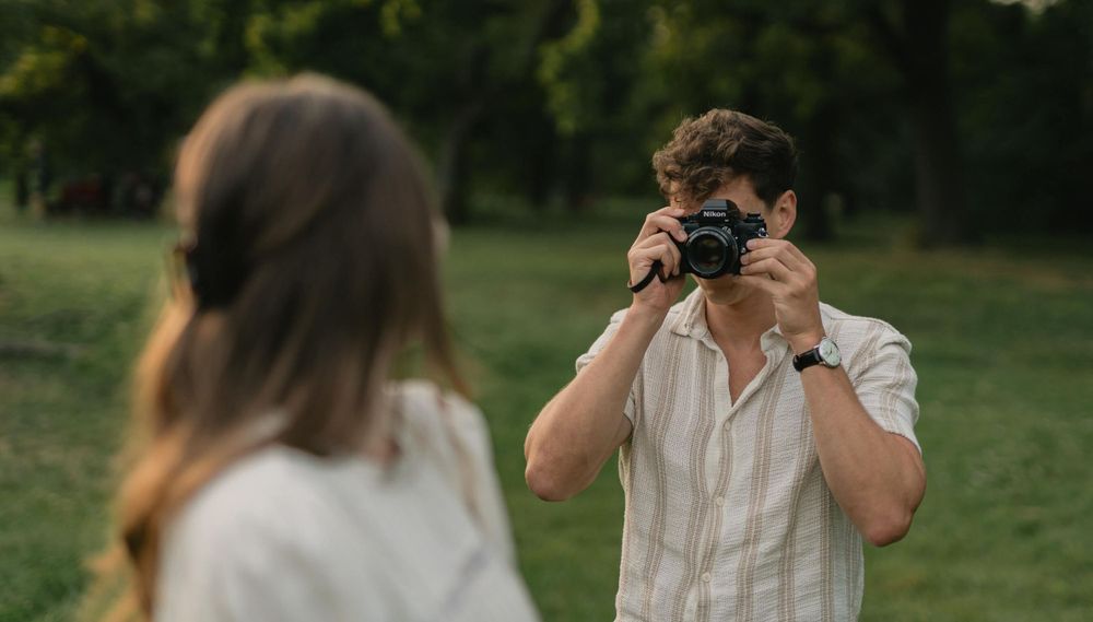 Person with vintage camera photographs their companion in an outdoor setting.