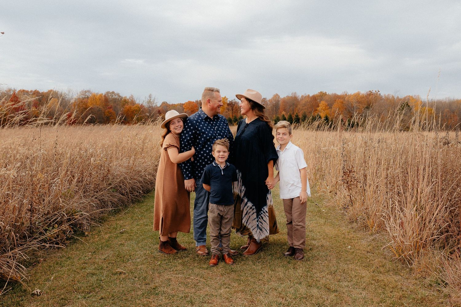 Family group walking together through a golden autumn field at sunset.