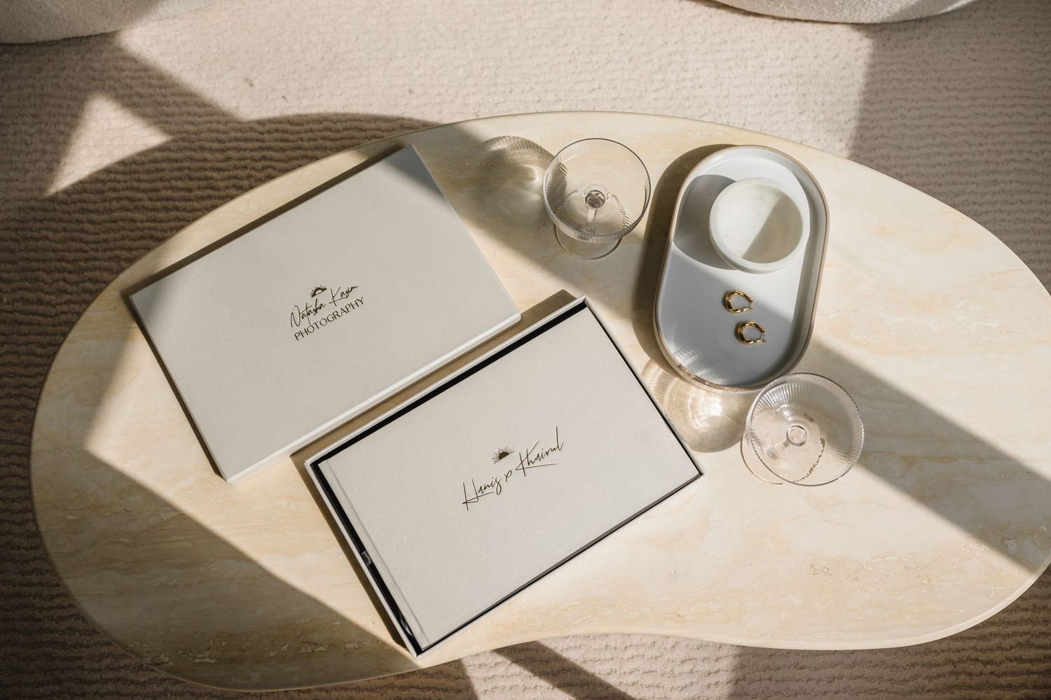Wedding album and stationery arranged on cream surface with dramatic natural lighting.