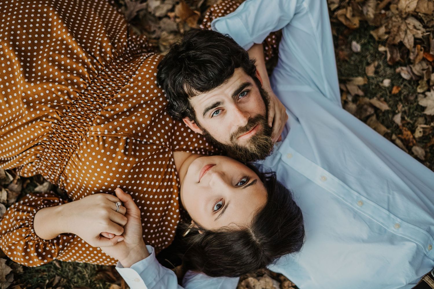 Couple laying on autumn leaves in blue and orange outfits during outdoor photoshoot.