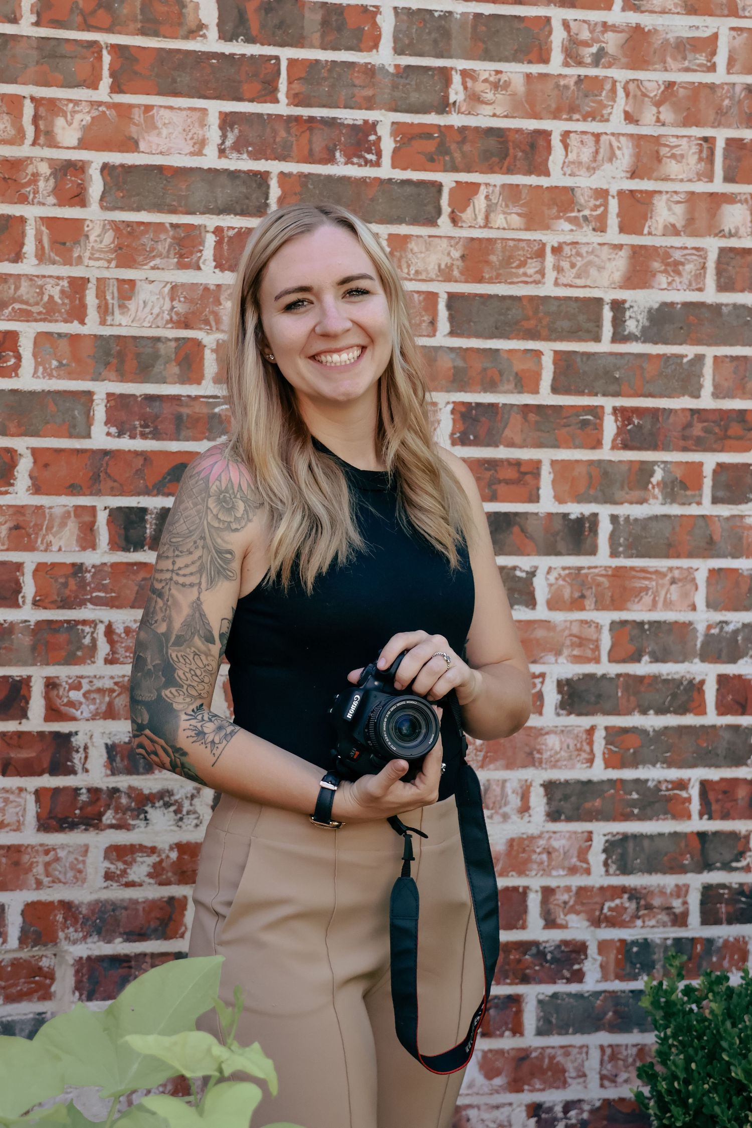 Professional photographer with camera posing against rustic brick wall backdrop.