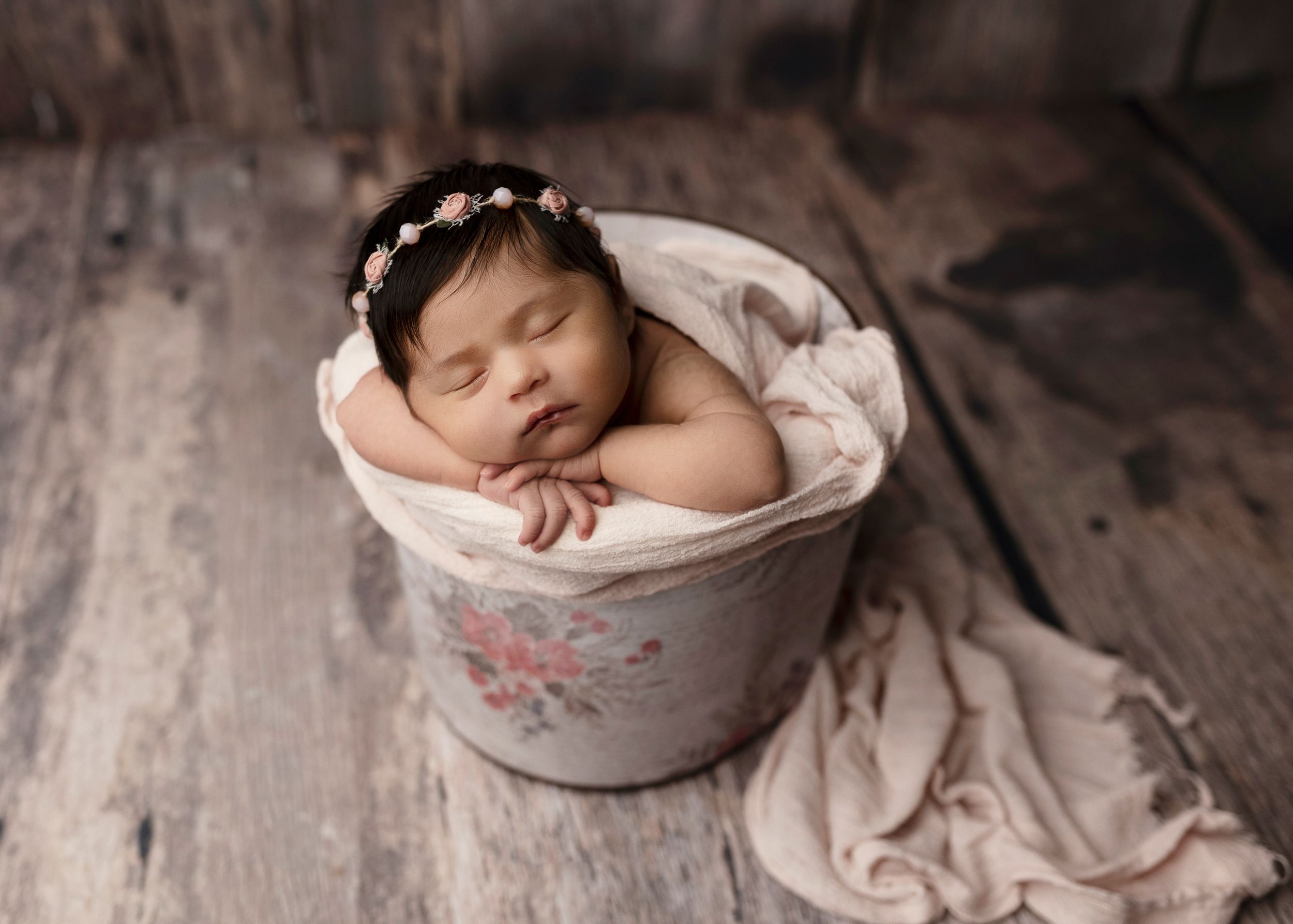 Sleeping newborn wearing flower crown posed in vintage bucket.
