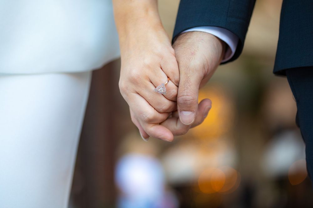 Close-up of intertwined hands with wedding rings against formal attire.