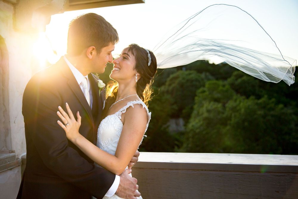 Bride and groom kissing on a sunny day with veil blowing in the wind