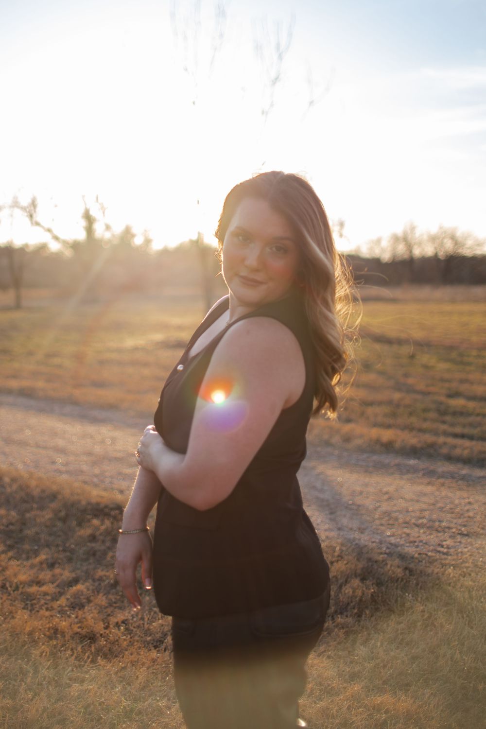 Side profile portrait of a woman in black dress with sun flare in background.