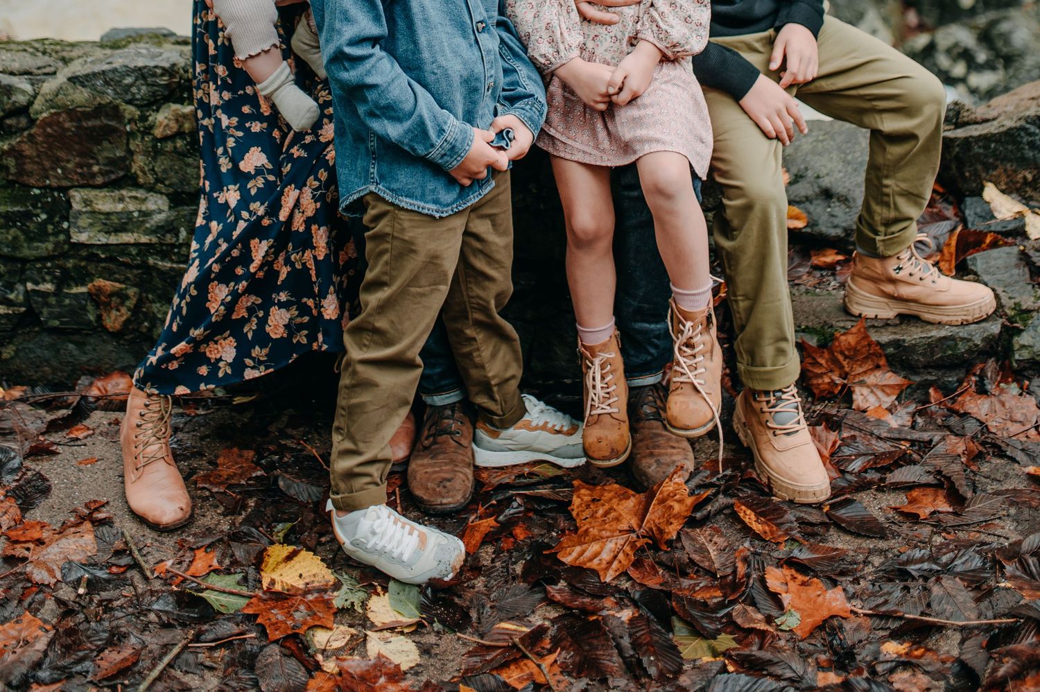 Close-up of family members' legs and boots standing on fallen autumn leaves.