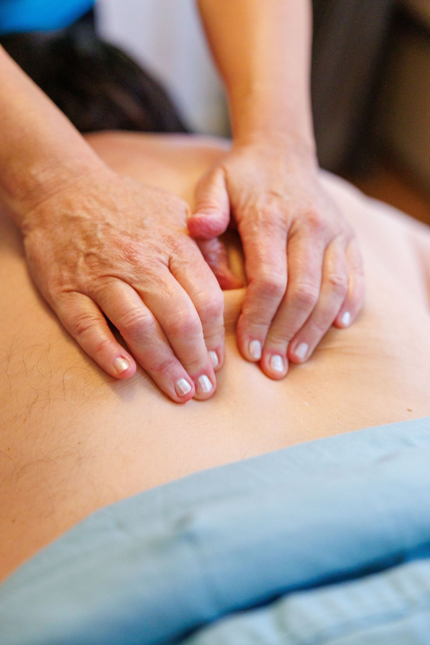 Close-up of hands performing therapeutic massage on back muscles with blue towel in background.