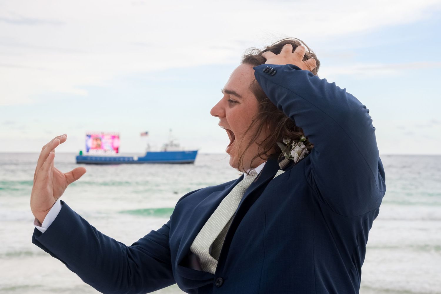 Expressive person in a suit gesturing dramatically with the ocean and ship in the background.