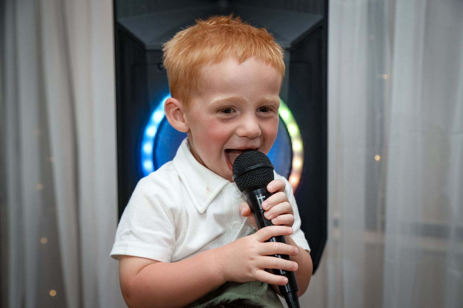 Young performer enthusiastically singing into a microphone at a wedding reception.