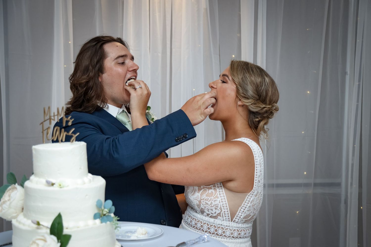 Playful moment of a couple feeding each other wedding cake during their reception.