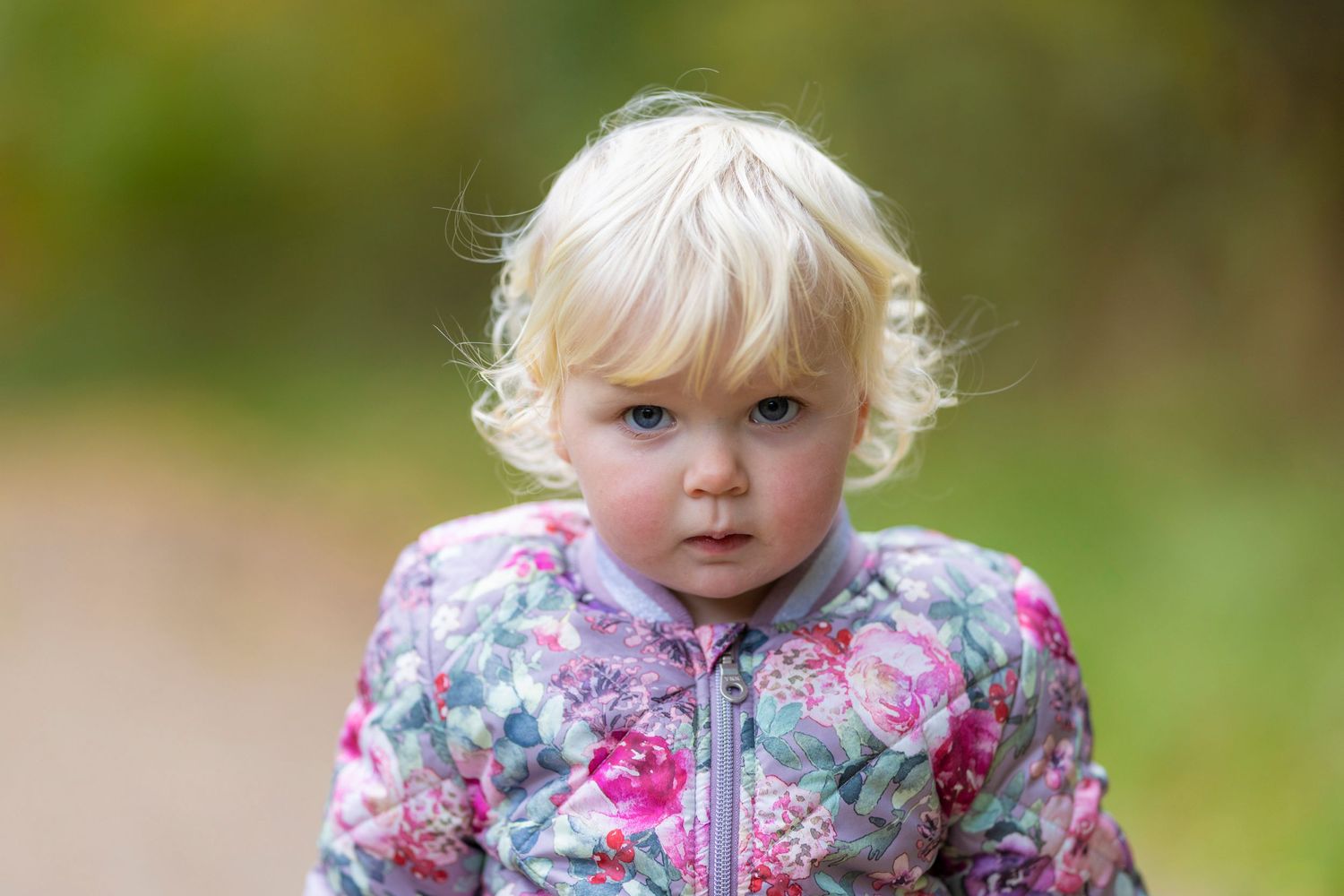 Child wearing floral patterned jacket outdoors in autumn setting.