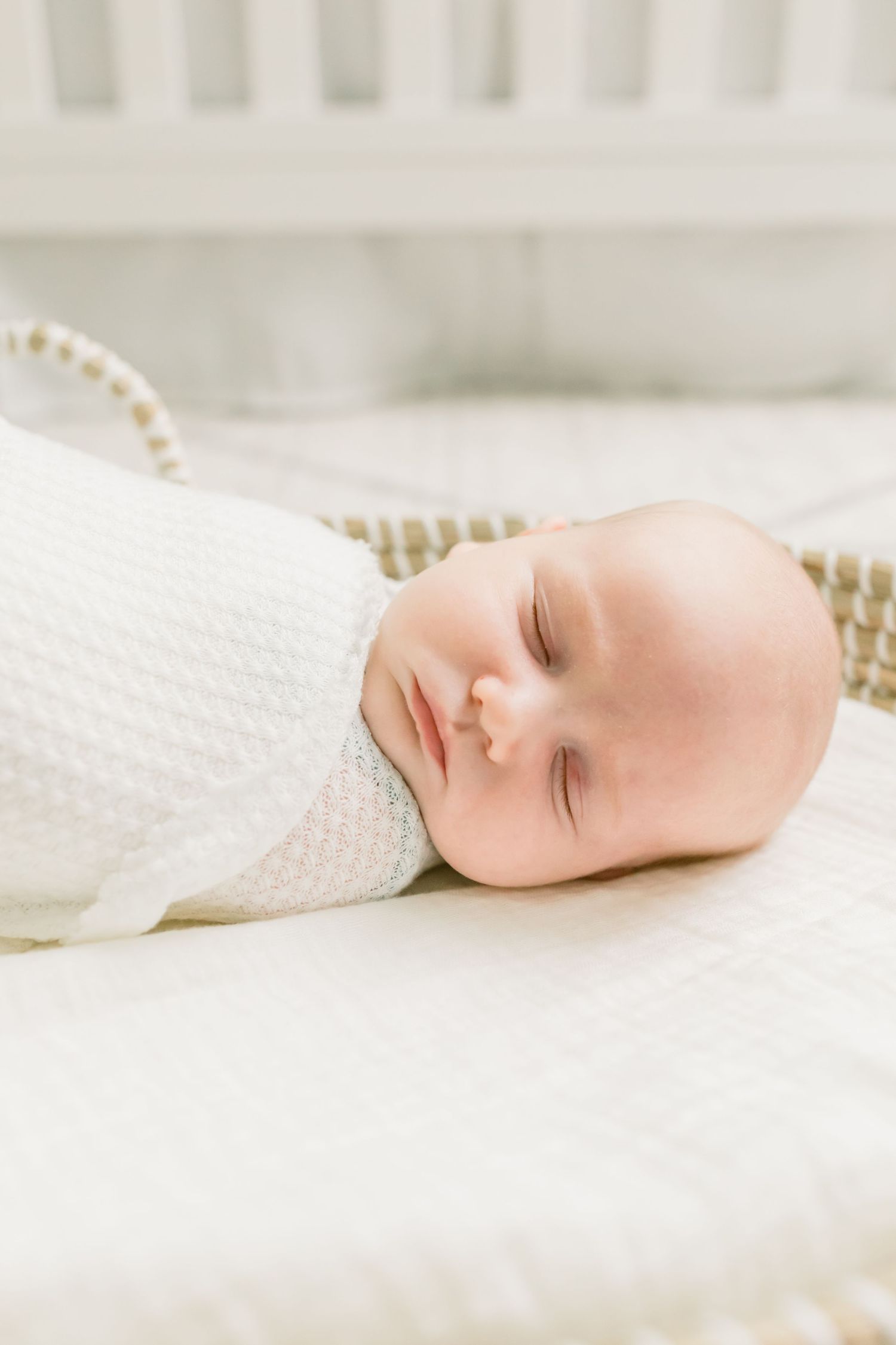 Peaceful sleeping infant in white knit swaddle on soft bedding.