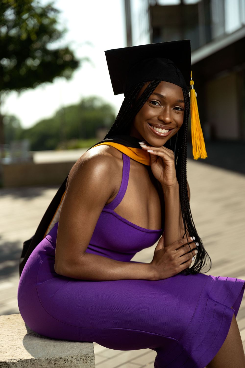 Graduate in purple dress and academic cap poses outdoors for celebration photos.