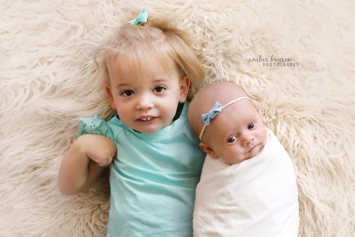Siblings in matching mint and white outfits lying on cream fur rug.