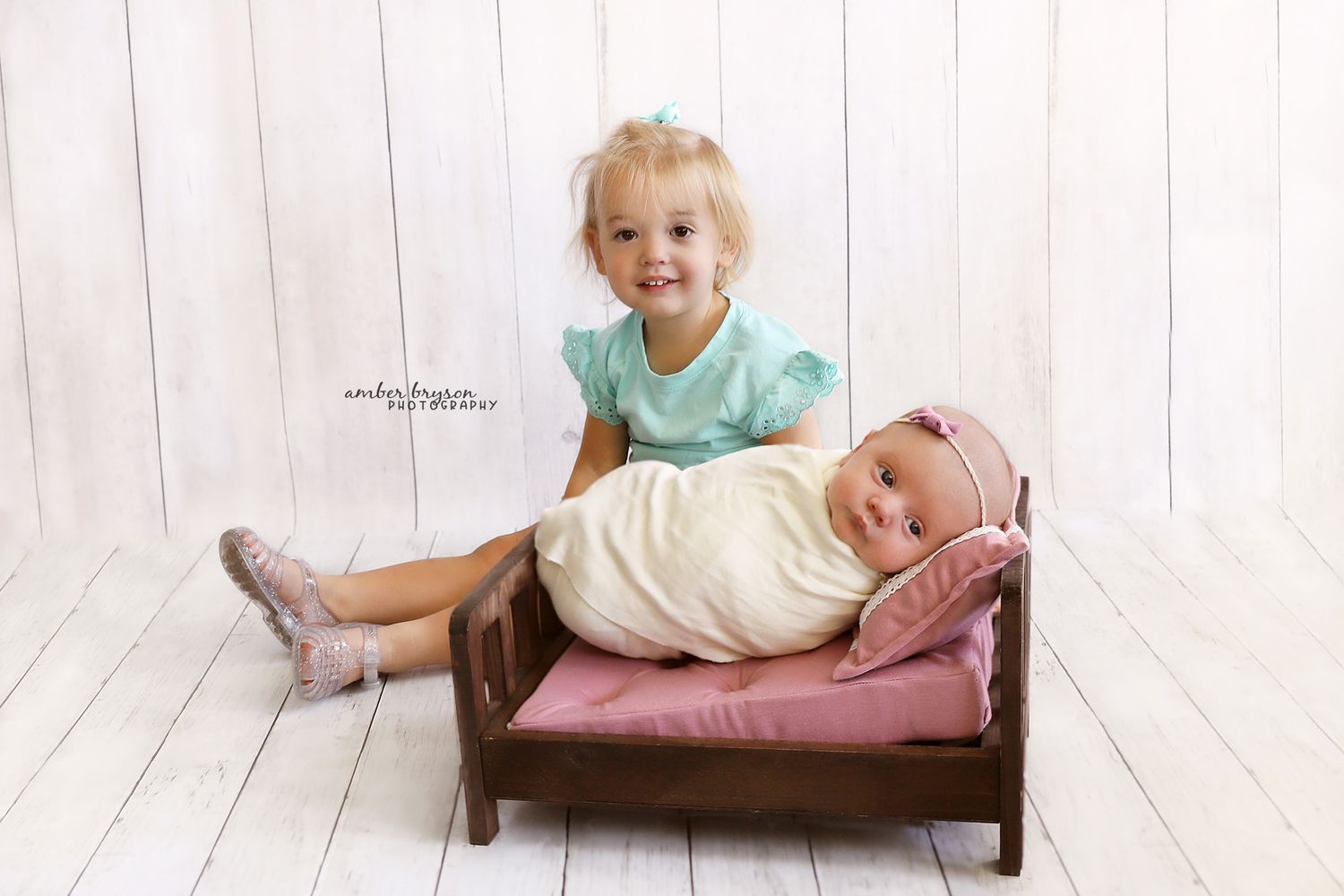 Two small children posing together on wooden bench against white background.