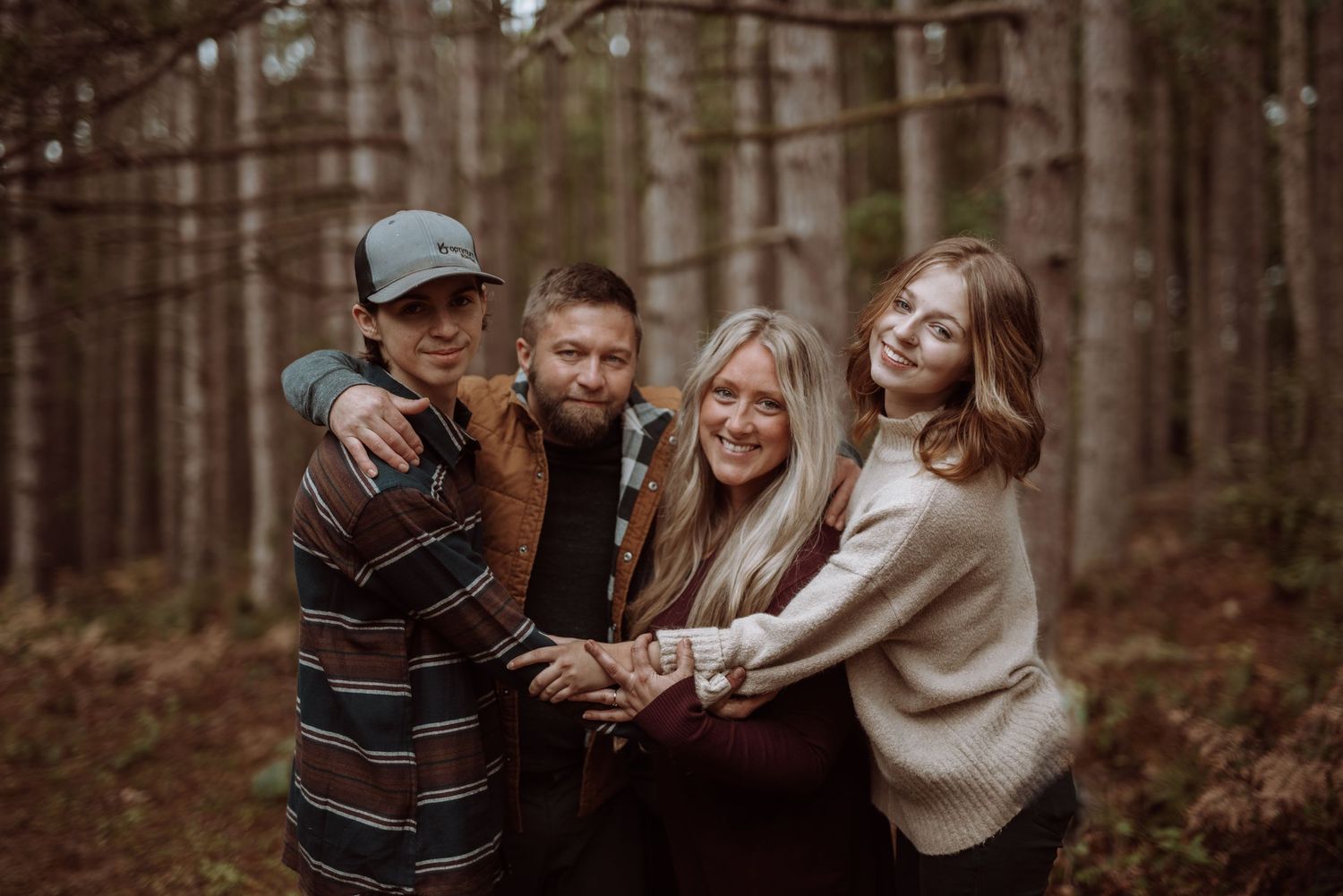 Four people pose together cheerfully in a pine forest setting.