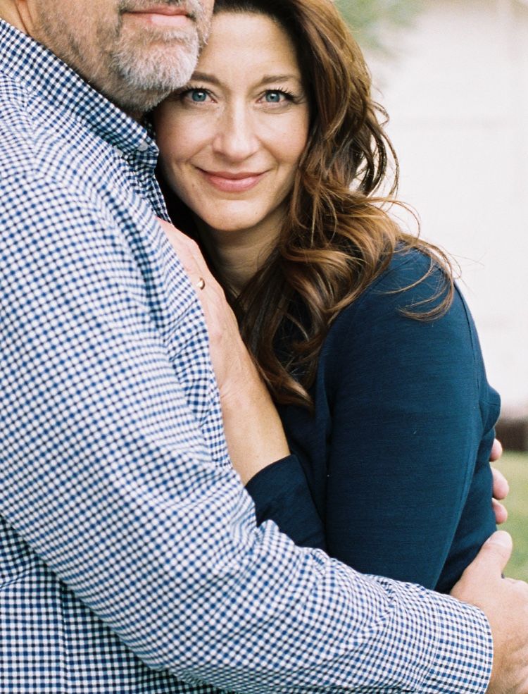 woman with long brown hair smiling at camera while  leaning against man