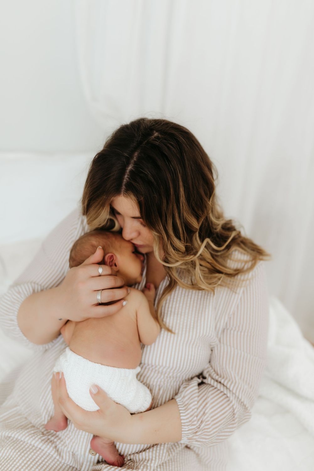 Intimate moment of parent in cream sweater snuggling with newborn baby against white background.