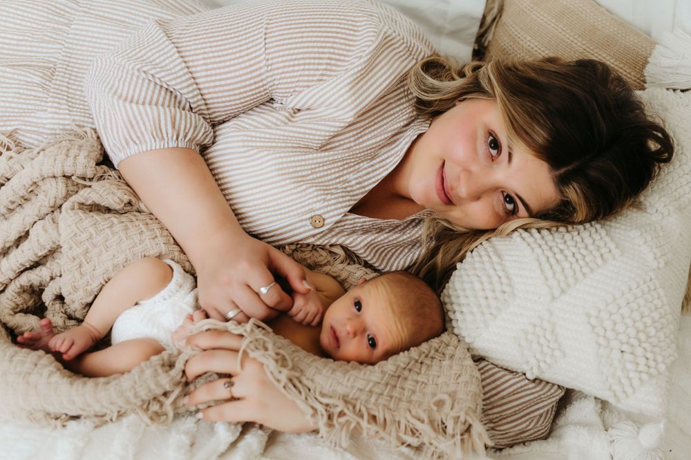 Parent and baby lying on white bedding with knit textiles in cozy indoor setting.