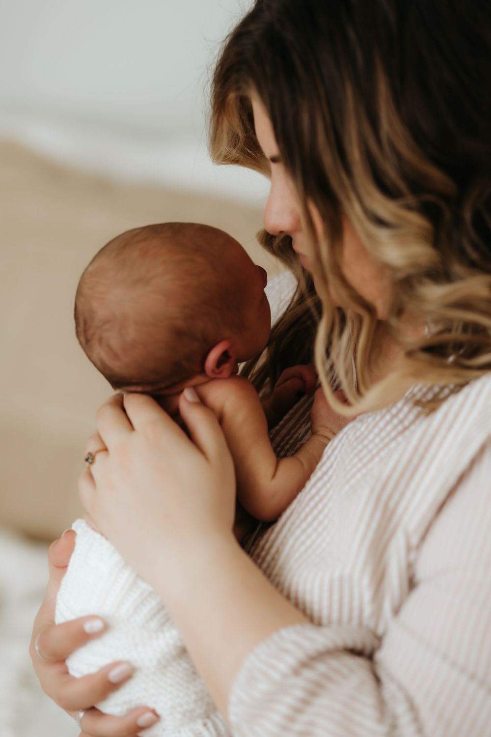 Parent tenderly cradling a newborn baby while wearing a cream knit sweater in soft natural lighting.