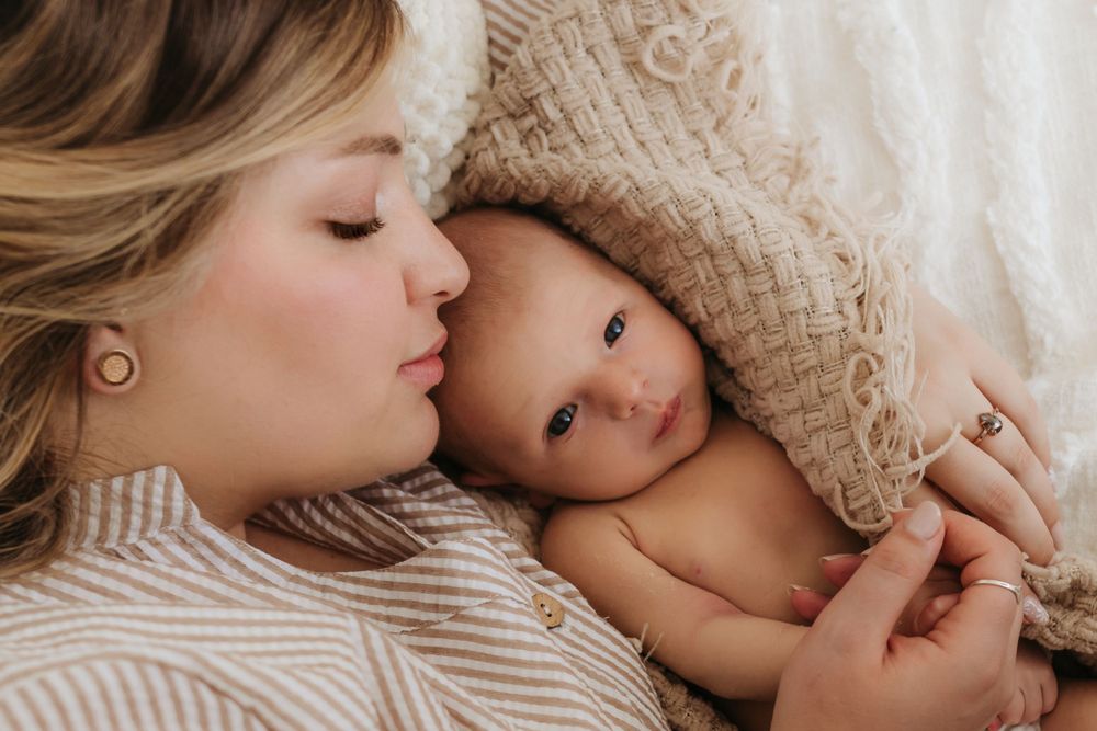 Intimate portrait of parent and alert newborn sharing tender moment under knit blanket.