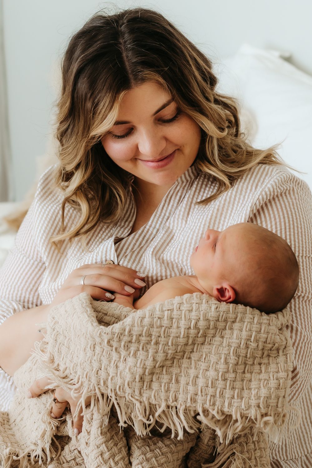 Parent in cream sweater gazing lovingly at newborn wrapped in textured blanket.