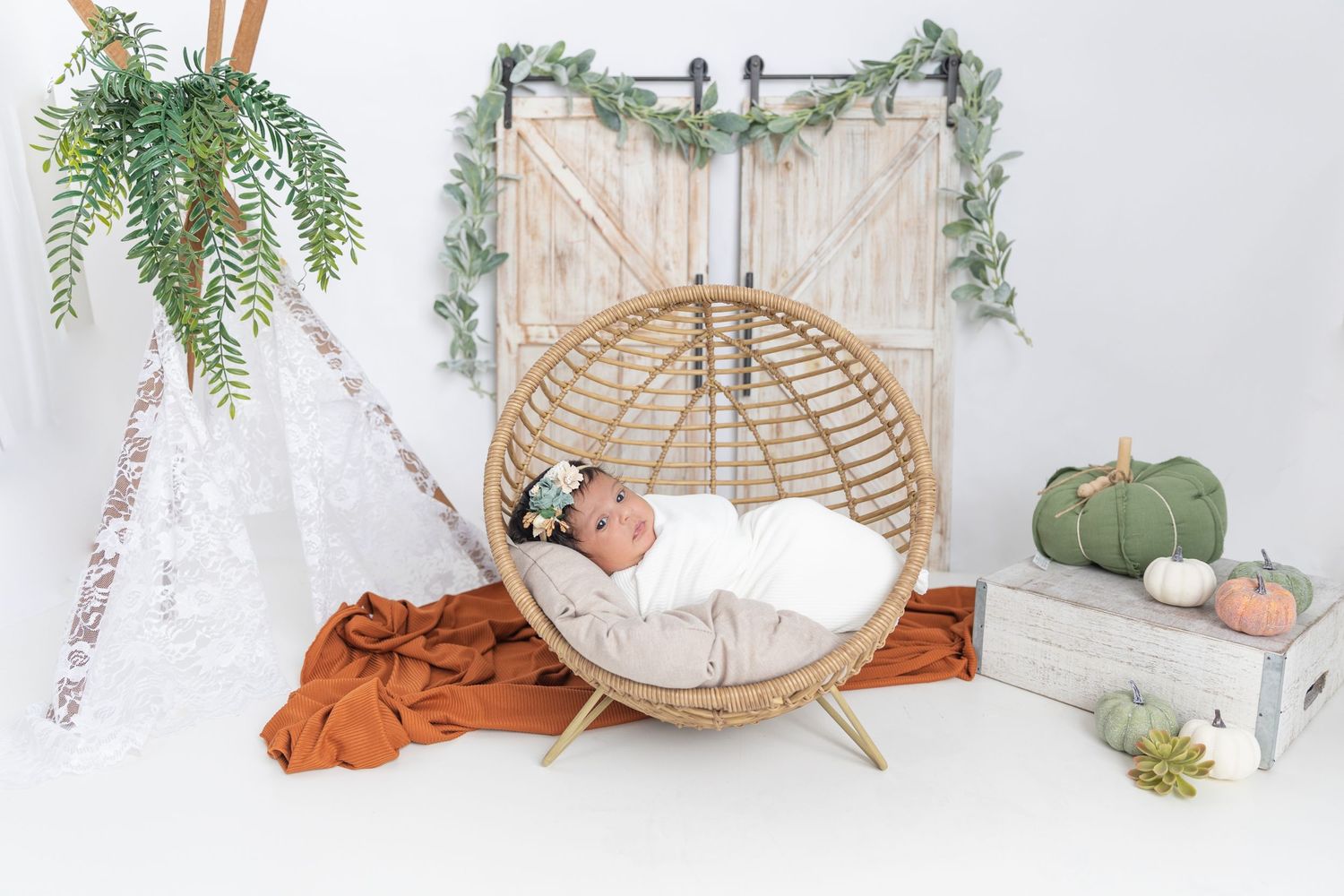 Dreamy nursery setup with hanging rattan chair, white fabric draping, and sage green pumpkin accents.