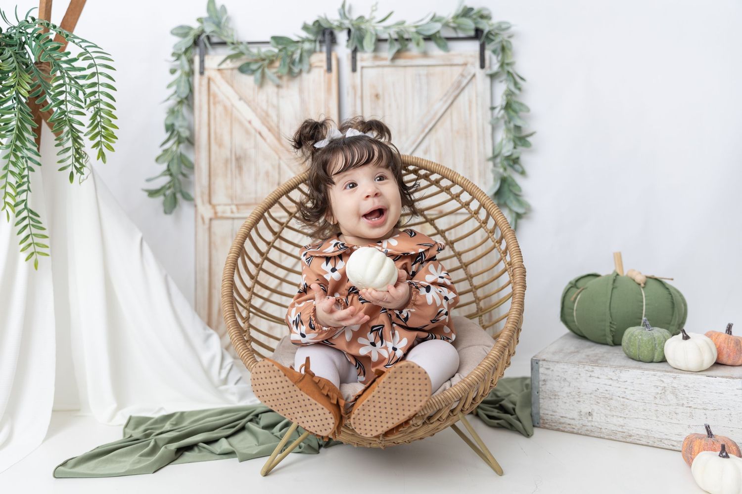 Studio scene with hanging rattan chair against rustic barn door backdrop with seasonal decor.