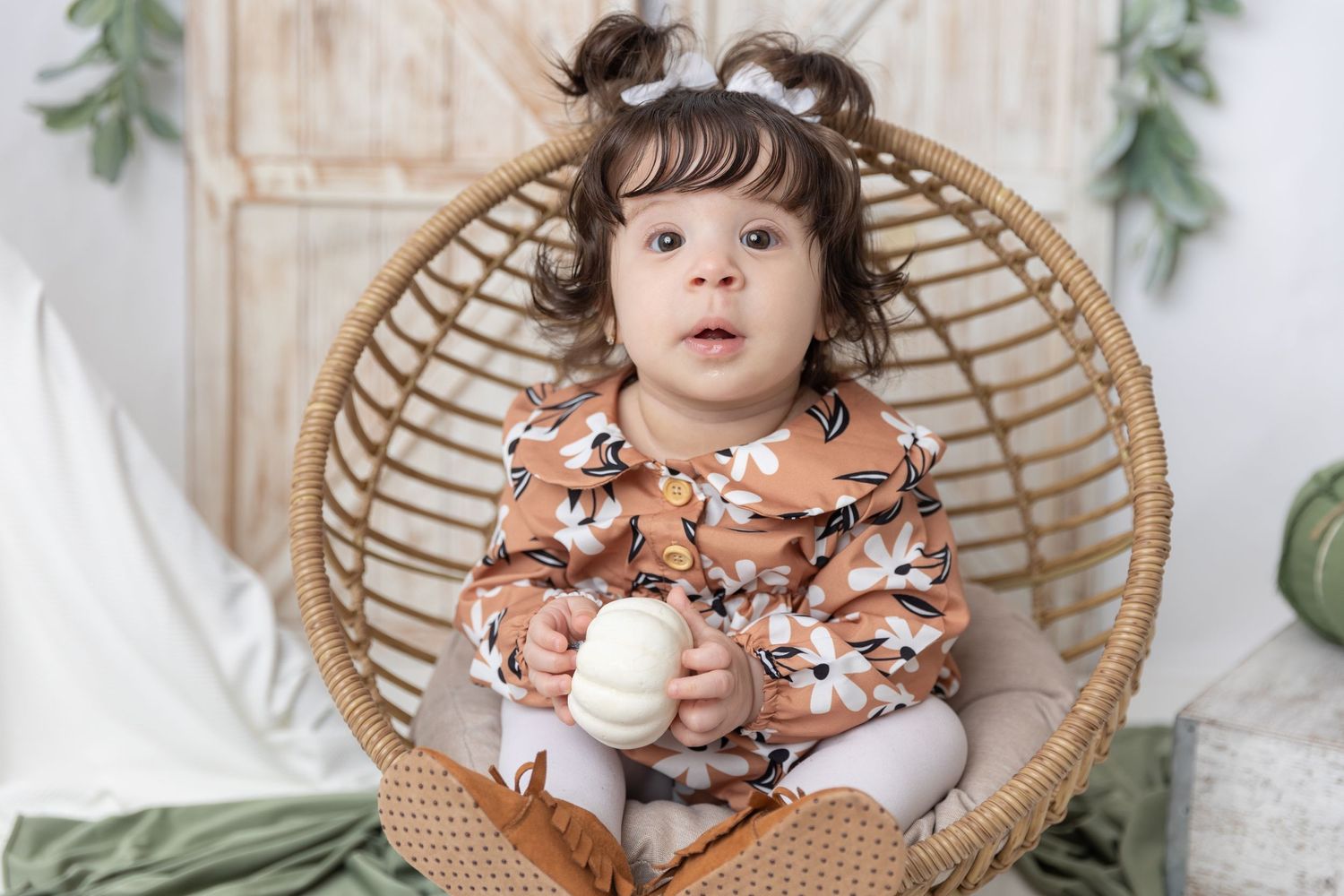 Cozy autumn scene with rattan chair, floral outfit, and decorative white pumpkins.