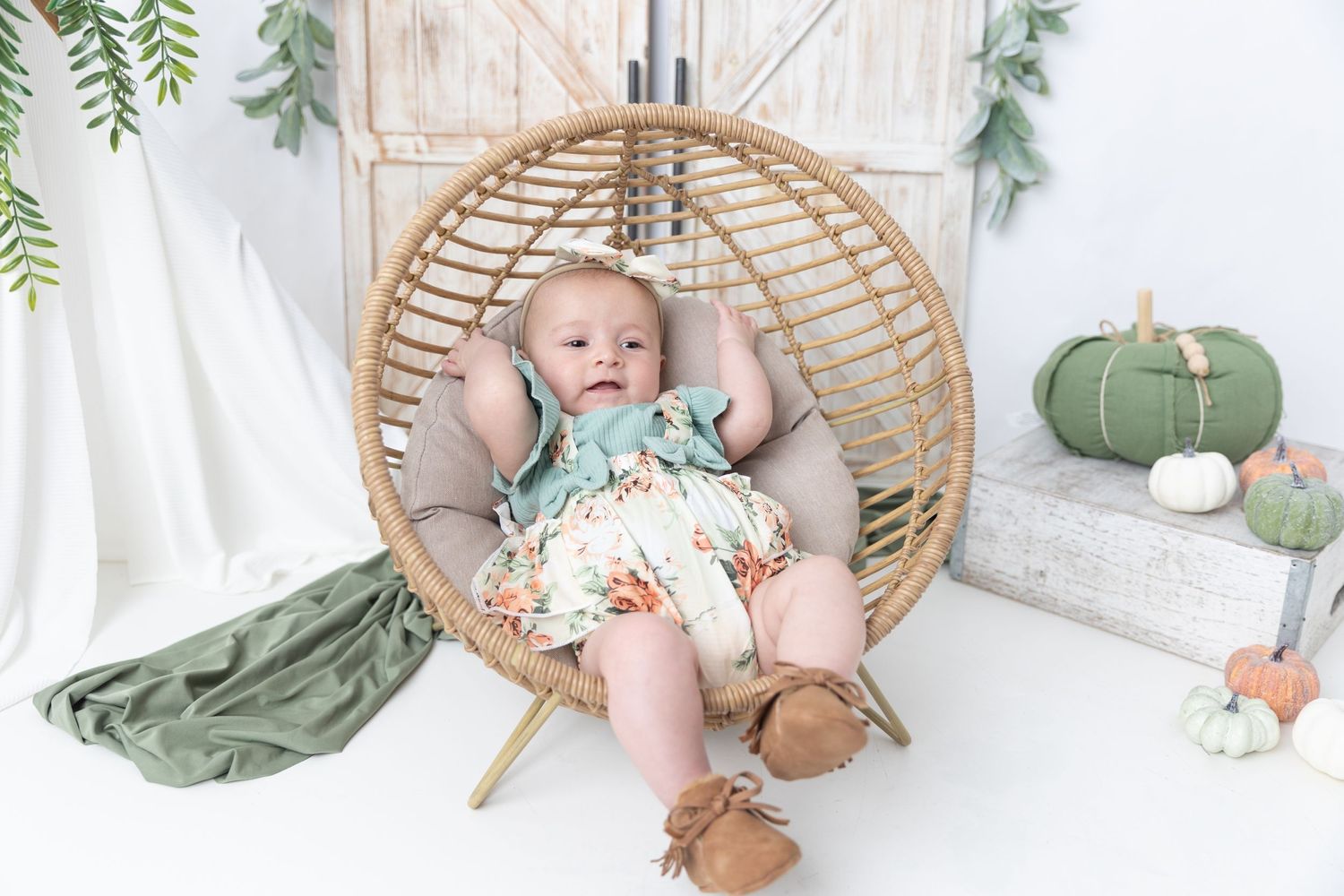 Cozy autumn photo setup with hanging rattan chair, barn door, and sage green pumpkin decor.