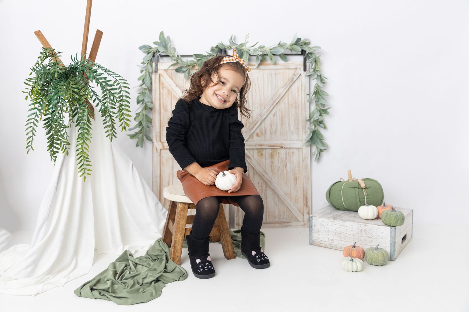 Studio photo setup with rustic door background, wooden stool, and decorative green pumpkins.