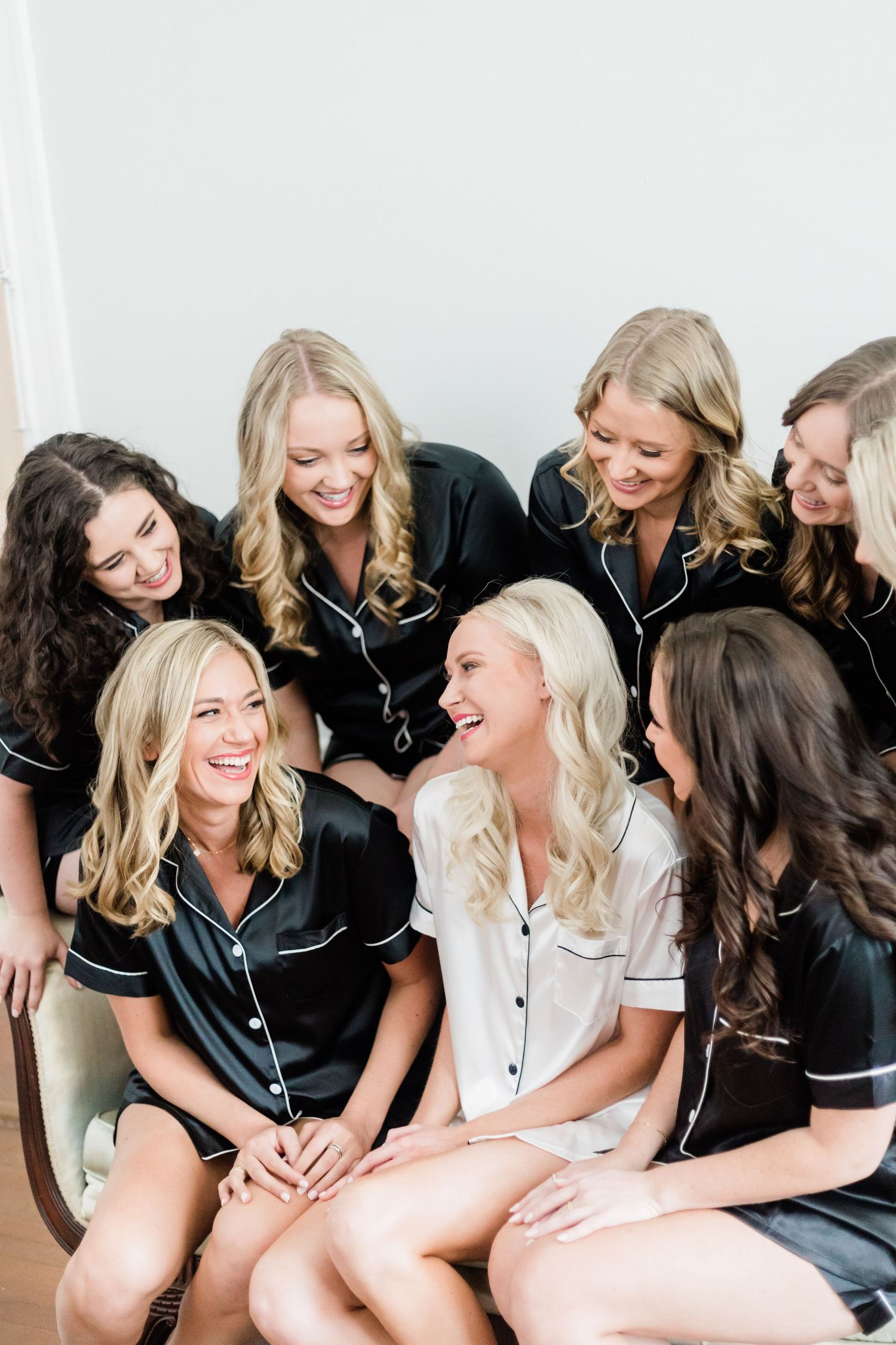 Group wearing matching black satin pajamas sharing laughter during pre-wedding preparations.