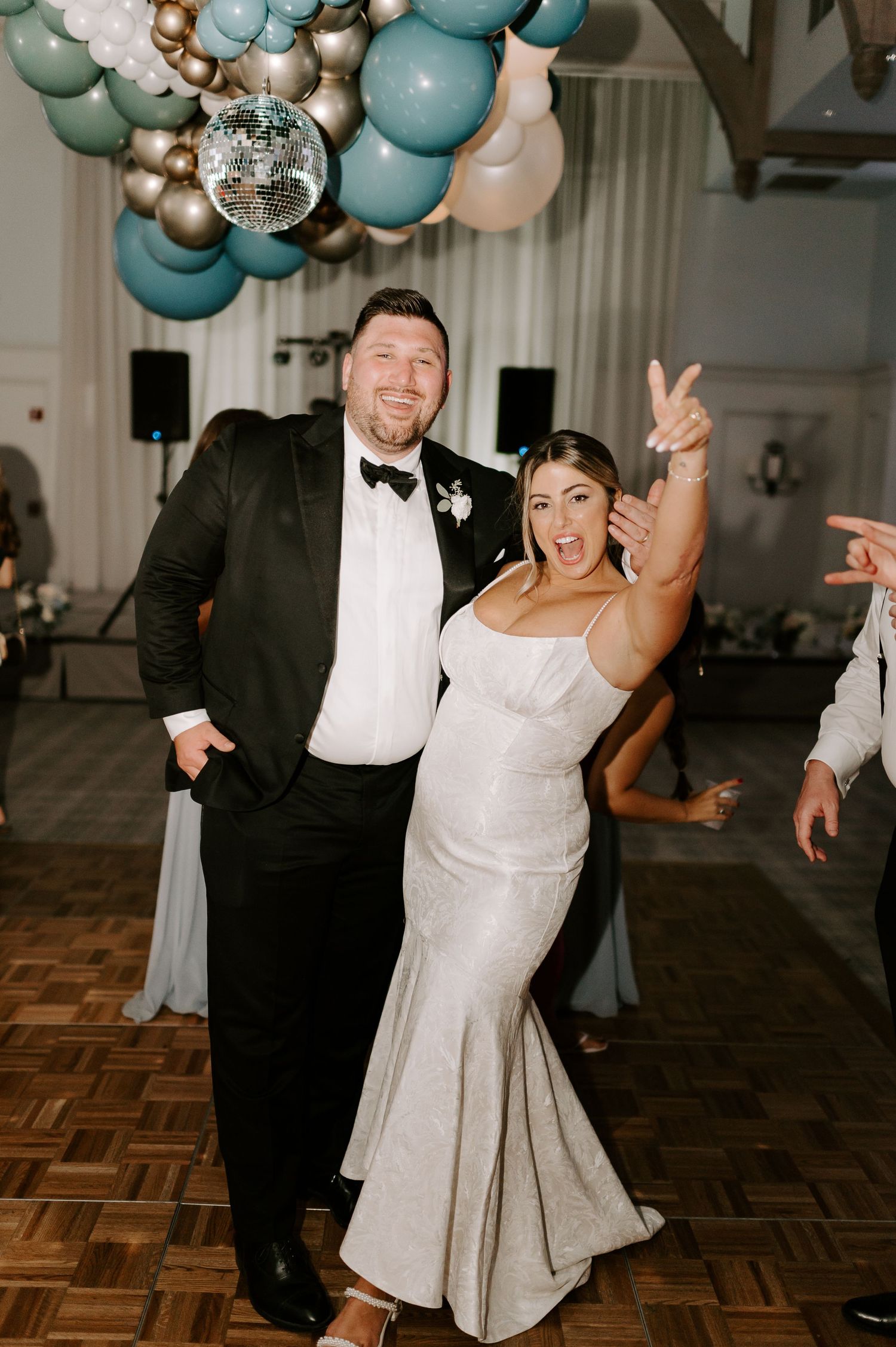 A couple dances joyfully under blue and silver balloons at their wedding reception.