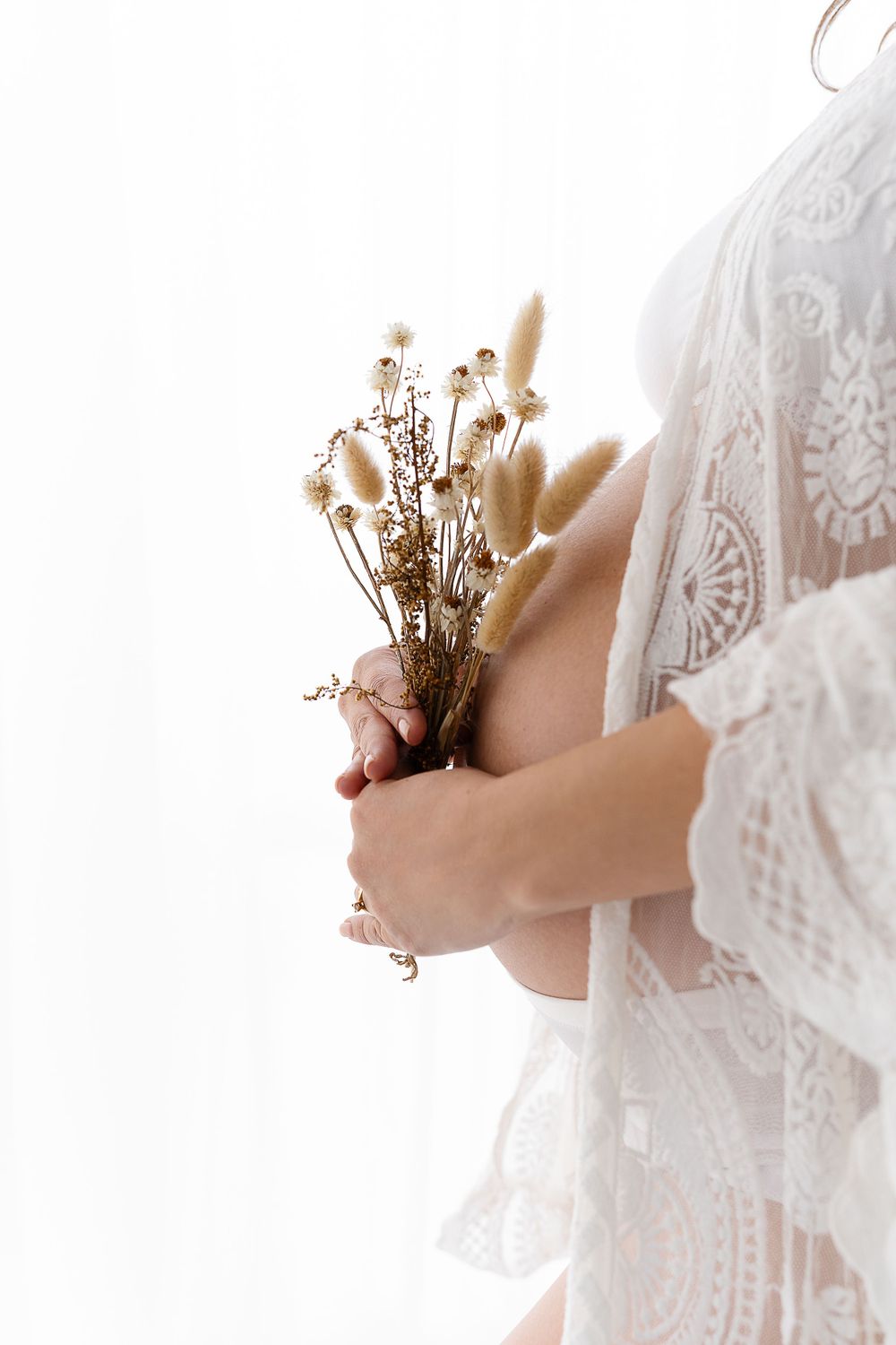 Close up of dried flowers held against lace fabric in maternity photoshoot.