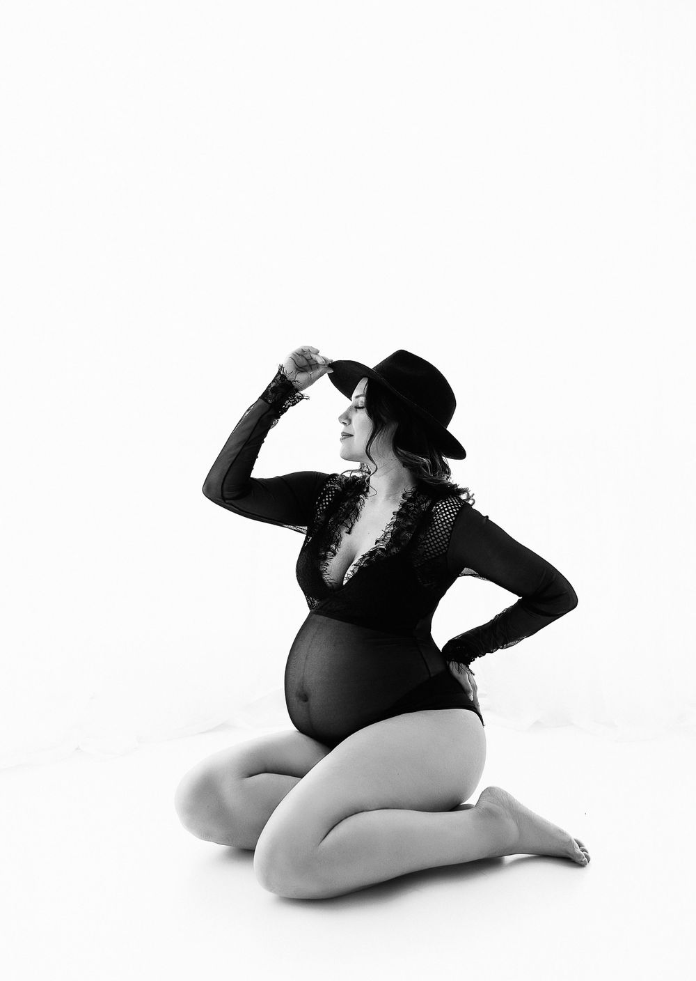 Silhouette of pregnant woman in black bodysuit and hat posing on white background.