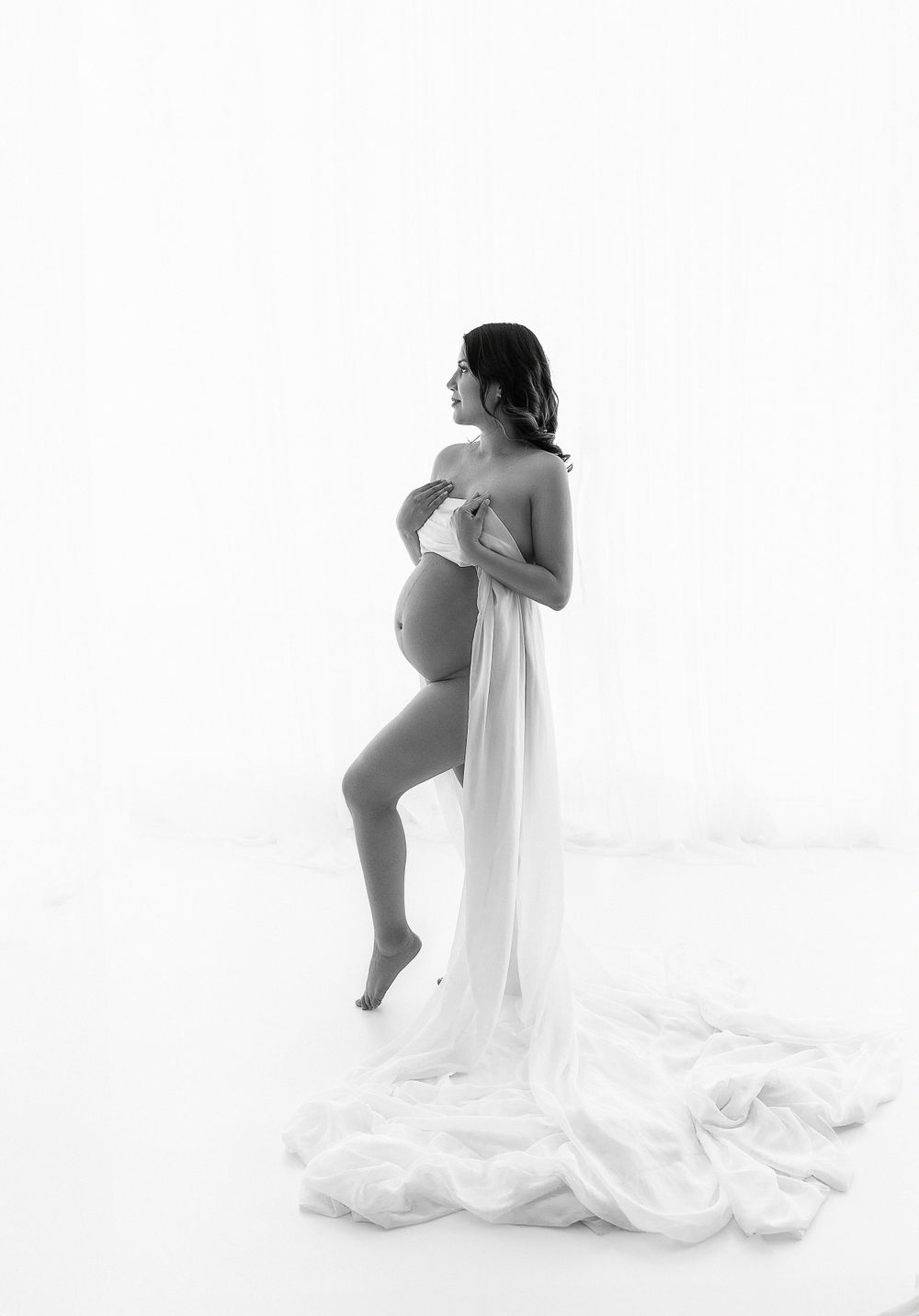 Artistic maternity photo with flowing white fabric against minimalist background.