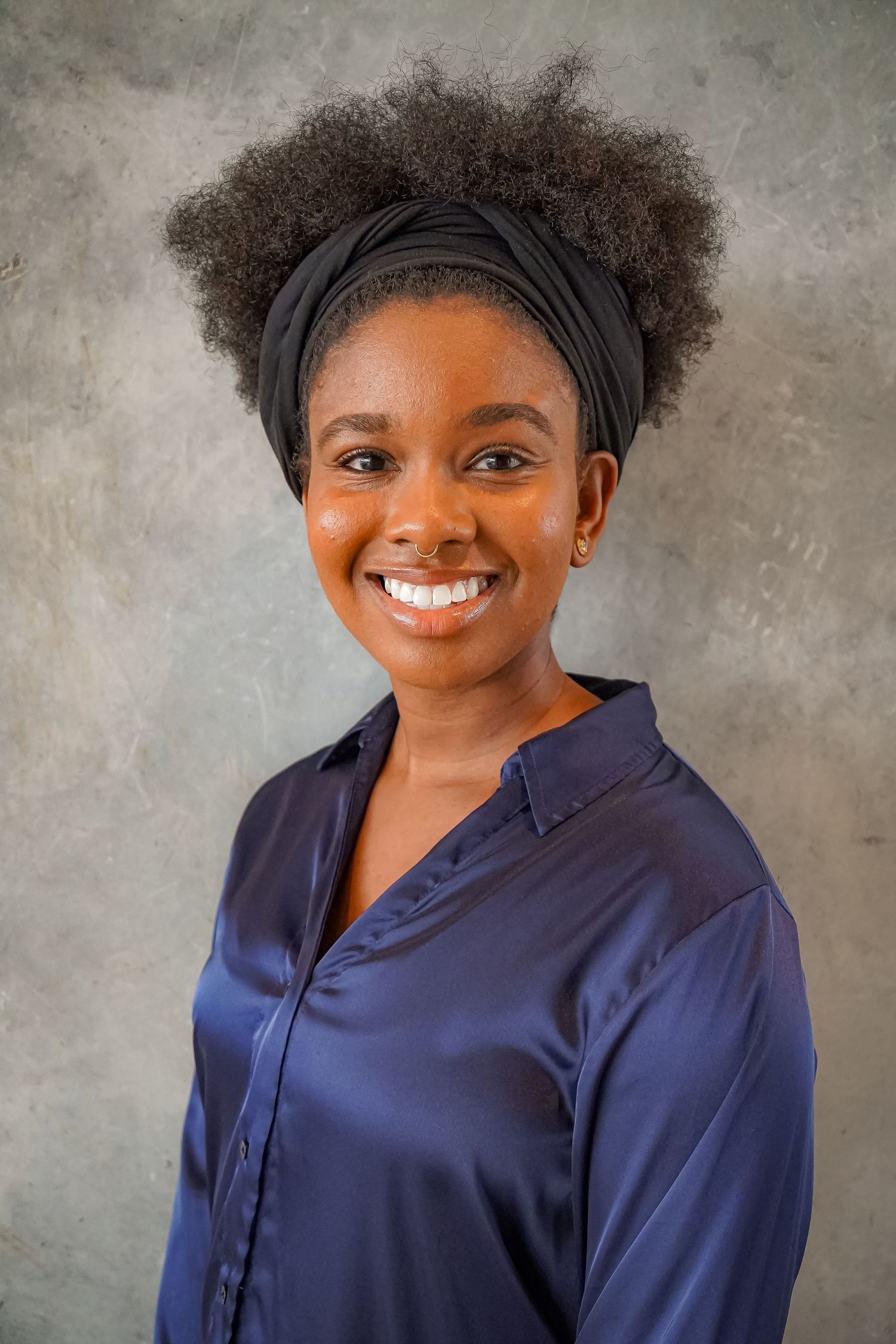 Professional portrait of person in navy top with natural hair against gray background.