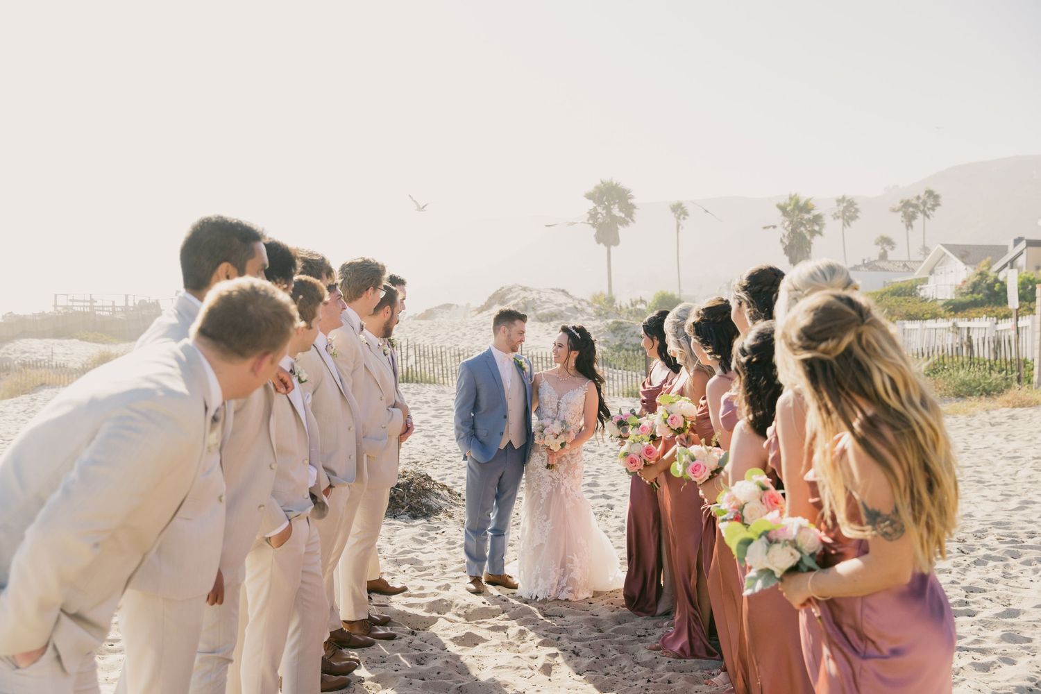 Wedding party celebrating on a scenic beach with palm trees in the background.